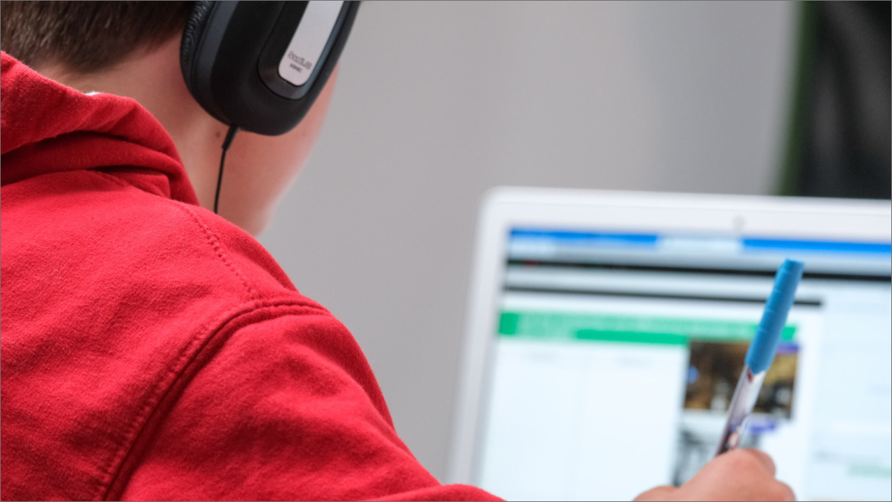 boy with headphones in front of the computer holding a pen