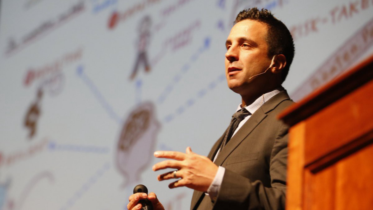 George Couros speaking on the stage by a podium